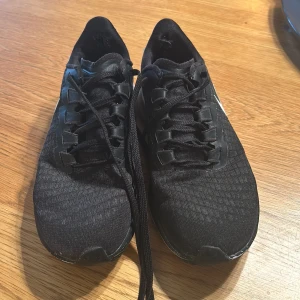 Svarta Nike löparskor - Säljer ett par svarta Nike löparskor i storlek 37. Skorna har en stilren design med snörning och är perfekta för träning. De är i välanvänt skick men fortfarande bekväma och funktionella. Perfekta för dig som vill ha ett par pålitliga träningsskor.