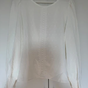 Vit blus med spetsdetaljer - Säljer en superfin vit blus med spetsdetaljer framtill. Den har långa ärmar med elastiska muddar som ger en luftig och elegant känsla. Perfekt för både vardag och fest! 💫