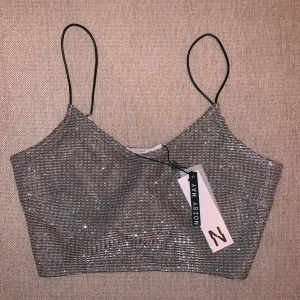 Glittrig topp från Noisy May - Säljer en superfin glittrig topp från Noisy May med tunna axelband. Toppen är i en silverfärg och har en croppad passform. Helt ny!