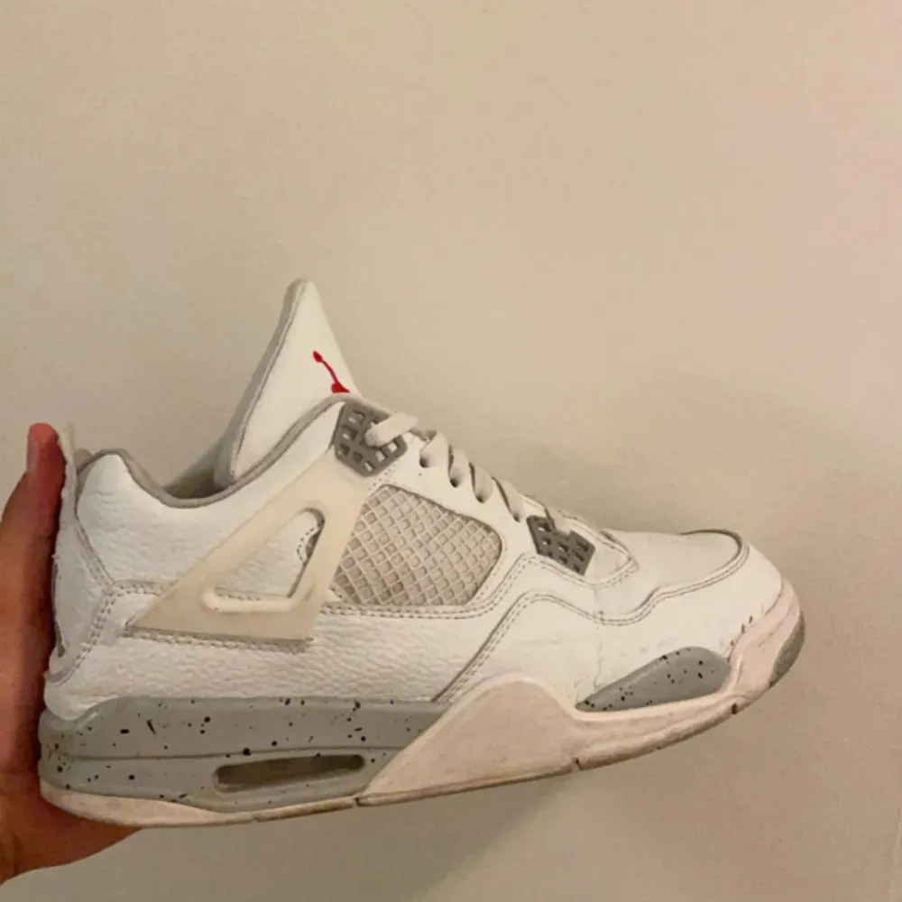 Säljer ett par vita Nike Air Jordans 4 i bra skick. De har en snygg design med grå detaljer och den klassiska röda loggan under sulan. Perfekta för både vardag och fest!. Skor.