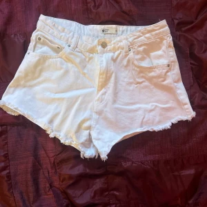 Vita jeansshorts från Garage - Säljer ett par snygga vita jeansshorts från Gina. De är högmidjade och har en fräsch fransig kant längst ner. Perfekta för sommardagar eller en avslappnad dag på stan. De har klassiska fem fickor och en knappgylf. Superbekväma och lätta att matcha 