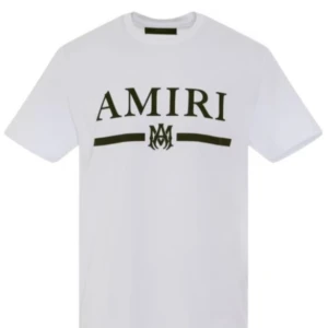 Vit t-shirt från Amiri - Säljer en snygg vit t-shirt från Amiri med deras ikoniska logga tryckt i svart på framsidan. T-shirten är i bomull och har en normal passform. Perfekt för en stilren och avslappnad look!