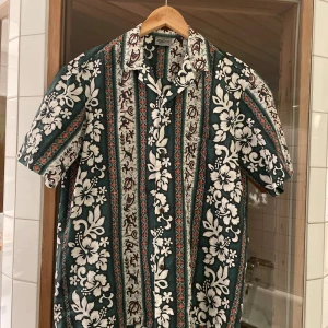 Grön och vit blommig skjorta från Royal Creations - Säljer en hawaii skjorta med vita blommor och mönster från Royal Creations. I nyskick.