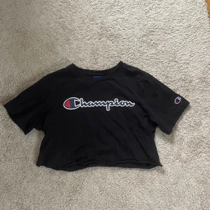 Svart croppad t-shirt från Champion - Säljer en svart croppad t-shirt från Champion. Den har det klassiska Champion-loggan tryckt på framsidan och en mindre logga på ärmen. T-shirten är i storlek Large men köpt fr barnavdelningen så är som en 34/36a, fint skick