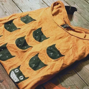 Orange t-shirt med kattmotiv - Säljer en cool orange t-shirt från Crosshatch med ett unikt kattmotiv. T-shirten har ett tryck av flera svarta kattansikten och texten 'BE DIFFERENT'. Perfekt för dig som vill sticka ut med en rolig och annorlunda stil!