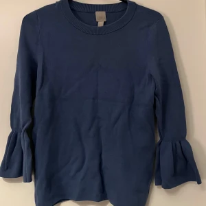 Mörkblå tröja med volangärmar - Säljer en superfin mörkblå tröja med volangärmar. Den är perfekt för både vardag och lite finare tillfällen. Tröjan har en rund hals och är i ett mjukt material som känns skönt mot huden. Passar perfekt till höst och vår!