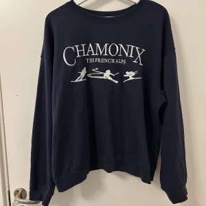 Mörkblå sweatshirt från H&M - Säljer en mörkblå sweatshirt från H&M med texten 'Chamonix The French Alps' och skidmotiv på framsidan. Tröjan har långa ärmar och en rund halsringning. Storleken är L men jag skulle säga att den passar bättre för S eller M. 