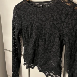 Svart spetsblus från ONLY - Snygg svart spetsblus från ONLY med långärmad design. Blusen har ett blommigt mönster och en elegant rund halsringning. Perfekt för att ge en stilfull touch till din outfit.