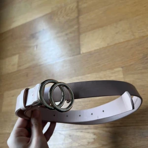 Ljusrosa  bälte med dubbla ringar - Snyggt ljusrosa bälte med stilrena dubbla ringar i metall. Perfekt för att ge en extra touch till din outfit. Justerbar längd för bästa passform.