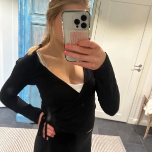 Svart omlottopp - Snygg svart omlottopp med långa ärmar och knytning i sidan. Perfekt för en stilren look. Svart med knytning på sidan ifrån gina tricot i storlek m men sitter som en s!🥰🥰knappt använd!