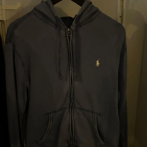 Blå hoodie från Ralph Lauren - Säljer en snygg blå hoodie från Ralph Lauren med dragkedja och klassisk logga på bröstet. Tröjan har en justerbar huva och praktiska fickor framtill. Bra skick och inga synliga slitage.