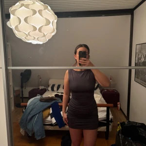 Mörkgrå tight klänning - Snygg mörkgrå klänning med tight passform och ärmlös design. Klänningen har en stilren look med öppen rygg som ger en extra touch. Perfekt för en kväll ute eller en speciell tillställning.