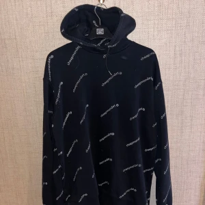 Svart hoodie från Cheap Monday - Säljer en svart hoodie från Cheap Monday med ett coolt mönster av märkets logga över hela tröjan. Den har en klassisk huva och långa ärmar.