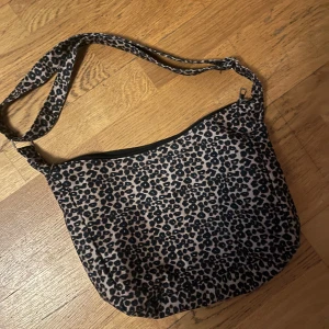 Leopardmönstrad axelväska - Snygg leopardmönstrad axelväska med dragkedja. Perfekt för att ge din outfit en cool touch. Väskan har ett justerbart axelband för bekväm passform.