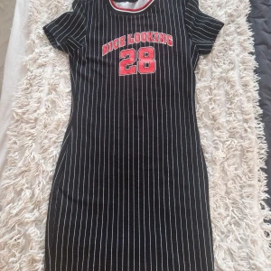 Svart randig klänning från Shein Oanvänd  - Säljer en svart klänning från Shein med vita ränder och röd text 'Nice Looking 28' på bröstet. Klänningen har korta ärmar och en sportig look. Perfekt för en avslappnad stil.