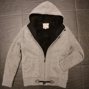 Pälsfodrad cardigan  - Säljer än väldigt mysig och tjock pälsfodrad cardigan. Mycket fint skick utan några som helst defekter. Extremt snygg och stilren med både dragkedja och knappar. Tröjan är grå med svart päls och fodring. Skriv vid minsta fundering!