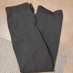 Grå kostymbyxor från Madlady - Snygga grå kostymbyxor från Madlady i en klassisk design. Byxorna har en rak passform och är perfekta för en stilren look. Ena sömmen har gått upp längst ner har gått upp men går lätt att fixa! 