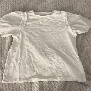 Vit topp från Zara - Säljer en söt vit topp från Zara med volangdetaljer vid ärmarna. Toppen har korta ärmar och är gjord i ett mjukt bomullsmaterial. Perfekt för en avslappnad stil.