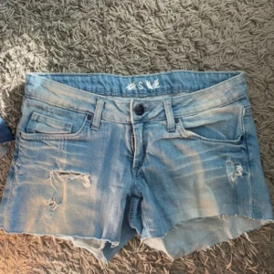 Blå jeansshorts med slitningar - Snygga blå jeansshorts med slitna detaljer och råa kanter. Perfekta för en avslappnad stil. De har en knapp och dragkedja framtill samt fem fickor. Inga defekter❤️