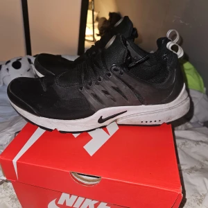 Svarta Nike Air Presto - Säljer ett par svarta Nike Air Presto sneakers. Skorna har en stilren design med snörning och en vit sula som kontrasterar mot det svarta. Perfekta för en sportig look. Priset kan diskuteras 