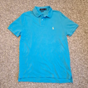 Ljusblå pikétröja från Polo Ralph Lauren  - Säljer nu denna stilrena ljusblåa pikétröja med gul logga från Polo Ralph Lauren. Custom slim fit, storlek M. Köpt i Volt butiken i Stockholm. Skick: 7/10