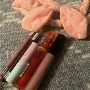 Sminkset med läpprodukter och hårband - Säljer ett sminkset med två läppennor från Maybelline i nude och vinröd, ett läppbalsam i pastellfärgad förpackning, W7 Hot Shot plumping oil och Technic Wet n Wild läppglans i rosa nyans. Inkluderar även ett mjukt rosa hårband med rosett.