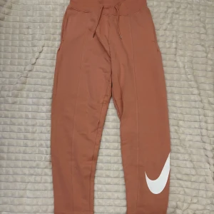 Rosa mjukisbyxor från Nike - Snygga bruna mjukisbyxor från Nike med en stor vit logga på benet. Byxorna har en bekväm passform i storleks. knappt använt