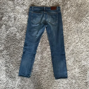 Tiger jeans 33/34 - Snygga blå jeans med en klassisk femficksdesign och en liten reva på ena benet för en trendig look. Byxorna har en knapp och dragkedja framtill samt en läderpatch på baksidan av midjan.