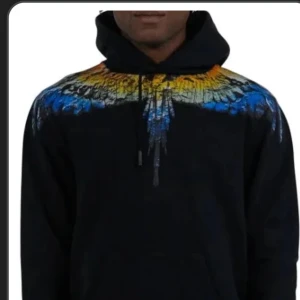 Svart hoodie med färgglatt mönster - Marcelo burlon! Köpt i emporia för 4499 men kan gå ner i pris vid snabb affär! Använder inte längre och står bara i garderoben. 9/10 i skick!   Snygg svart hoodie med ett färgglatt mönster i blått, gult och orange över axlarna. Perfekt för en cool och avslappnad stil. Hoodien har en klassisk passform med dragsko i huvan.