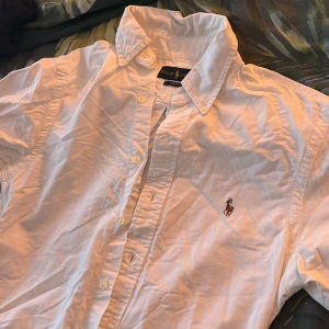 Vit klassisk  Ralph Lauren - Mitt i flytt så tyvärr inget strykjärn! Säljer en klassisk vit skjorta från Ralph Lauren med broderad logga på bröstet. Skjortan har en slim fit passform och är långärmad med knappar hela vägen ner. Perfekt för en stilren look.