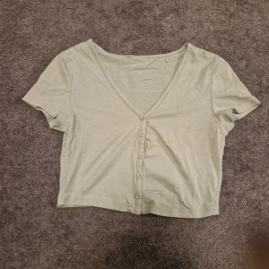 Ljusgrön kortärmad topp med knappar - Säljer en ljusgrön kortärmad topp med v-ringning och knappar framtill. Perfekt för en avslappnad stil.