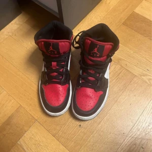 Nike Air Jordans i rött och svart - Snygga Nike Air Jordans i en klassisk färgkombination av rött, svart och vitt. Skorna har en hög modell med snörning och den ikoniska Jumpman-loggan på plösen. Perfekta för dig som vill ha en stilren och sportig look.