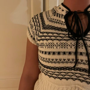 Svartvit stickad topp med knytband - Snygg svartvit stickad topp med korta ärmar och ett unikt mönster. Toppen har ett knytband vid halsen som ger en extra detalj. 🖤🖤 