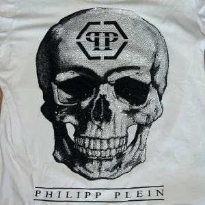 Philipp Plein tröja Vit/ döskalle  - Snygg vit t-shirt från Philipp Plein med en stor, glittrig dödskalle på framsidan. T-shirten har korta ärmar och är dekorerad med paljetter som ger en cool effekt. Perfekt för dig som vill sticka ut med en unik stil.