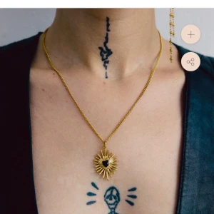 Guldhalsband med solhänge - Elegant guldhalsband med ett unikt solformat hänge. Hänget har en svart sten i mitten som ger en stilren kontrast. 