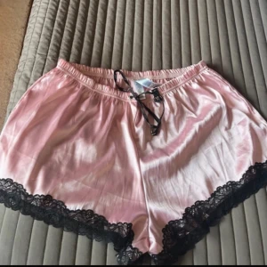 Rosa shorts med spetsdetaljer tror från new yorker storlek:XL - Säljer ett par söta rosa shorts med svarta spetsdetaljer längs kanterna. De har en bekväm elastisk midja med knytband framtill. Perfekta för en avslappnad och stilren look. aldrig använda och aldrig testade. Säljer för 75 kronor. 