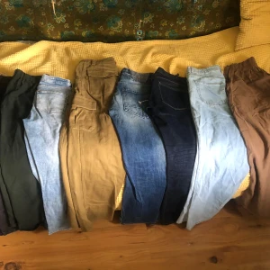Samling av olika byxor - En samling av olika byxor i varierande färger och stilar. Inkluderar jeans i ljus och mörk tvätt, samt cargopants i beige. Perfekt för att mixa och matcha till olika tillfällen.