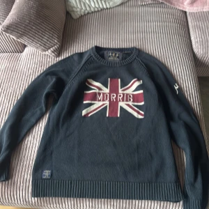 Mörkblå tröja från Morris - Säljer en snygg mörkblå tröja från Morris med ett stort Union Jack-motiv och texten 'Morris' på framsidan. Tröjan har långa ärmar och en broderad detalj med 'MG 1968' på ärmen. Perfekt för en stilren look. Storlek e Xl men passar även M och L 