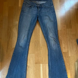 Blå bootcut jeans från Levi's - Snygga blå bootcut jeans från Levi's med klassisk femficksdesign och knappgylf. Jeansen har en lätt slitning för en avslappnad look och är perfekta för en casual stil. Levi's logotyp syns på bakfickan. Köpta i Paris för ca 2 år sedan och inga slitningar eller skador. Storlek 36/38