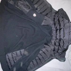 Moncler cardigan  - Säljer en snygg svart cardigan  från Moncler. Csrdiganen har en quiltad design med dragkedja och är perfekt för kyligare väder. Den har en stilren look och är tillverkad i syntetmaterial.