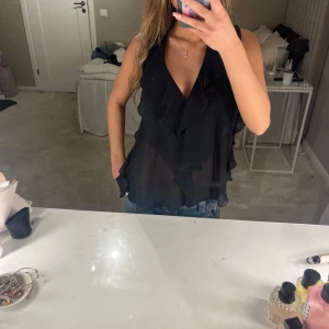 Svart ärmlös topp med volangdetaljer - Snygg svart ärmlös topp med volangdetaljer och knytning i nacken. 