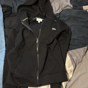 Svart hoodie med zip från Lacoste - Säljer en svart hoodie från Lacoste med dragkedja och klassisk passform. Passar bra på dig som är 175-180. 