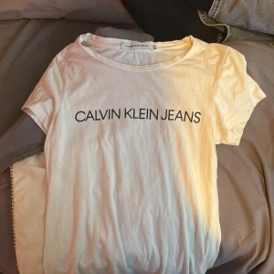Vit t-shirt från Calvin Klein Jeans - Säljer en stilren vit t-shirt från Calvin Klein med svart text på bröstet. Perfekt för en avslappnad look. T-shirten är i storlek xs och säljer den för att jag inte använder den. Köpte den för 600kr i höstas.