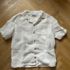 Vit kortärmad skjorta från Gabba - Snygg vit skjorta från Gabba i ett texturerat material. Skjortan har korta ärmar och knappar framtill. Perfekt för en avslappnad stil.