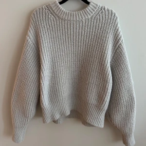 Grå stickad tröja - Mysig stickad tröja med en avslappnad passform. Perfekt för kyliga dagar med sin ribbade struktur och långa ärmar. En stilren och bekväm tröja som passar till det mesta.