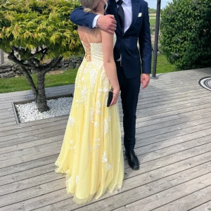 Gul dröm balklänning💛 - Säljer min underbara balklänning! Den har snörning i ryggen som gör att man kan välja själv hur hårt den ska sitta runt midjan och bysten💛Extra fina detaljer med vita blommorna som gör den helt perfekt🥹Den har även inlägg för brösten så bh behövs inte. Jag är 167cm och den är uppsydd efter min längd, passar ju även kortare och skulle nog även passa 170cm beroende på hur mycket släp man vill ha. Endast använd en gång, inte tvättad men de kan diskuteras vid intresse🤍