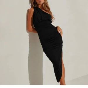 Svart oneshoulder klänning - Elegant svart oneshoulder klänning med draperad design och smickrande passform. Perfekt för en kväll ute eller en speciell tillställning. Klänningen har en stilren slits som ger en extra touch av glamour.