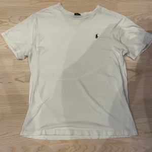 Vit t-shirt från Ralph Lauren - Säljer en klassisk vit t-shirt från Ralph Lauren med det ikoniska broderade logotypen på bröstet. T-shirten är tillverkad i 100% bomull och har en normal passform. Och de är ett litet hål på framsidan men inget man ser på långt håll bara om man kollar riktigt nära. Storlek M i vuxen. Perfekt för en stilren och avslappnad look.