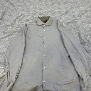 Grå skjorta från Hugo Boss - Säljer en stilren grå skjorta från Hugo Boss i slim fit. Skjortan har långa ärmar och knappar framtill. Perfekt för en elegant look.