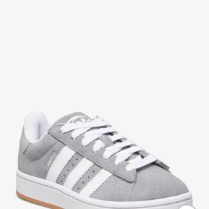 Grå Adidas campus  - Snygga grå sneakers från Adidas med klassiska vita ränder och snörning. Perfekta för en avslappnad stil. Skorna har en vit sula med en brun detalj på undersidan.